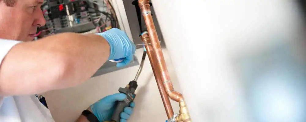 Water heater repair technician testing copper pipe connections and controls in San Diego, CA